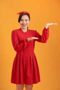 Turuncu arka planda el hareketi yapan Asyalı genç bir kadın.