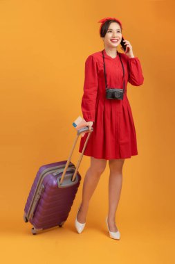 Genç Asyalı kadın çantasıyla turuncu arka plan üzerinde izole edilmiş bir telefon kullanıyor..