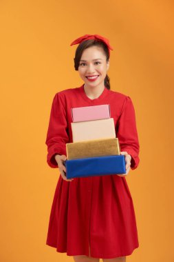 Gülümseyen Asyalı genç bayan turuncu arka planda izole edilmiş hediye kutularını tutuyor..