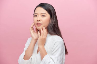 Güzel Asyalı genç bir kadın yumuşak yanak gülümsemesine dokunuyor. Temiz ve taze tenli. Mutluluk ve neşe dolu.