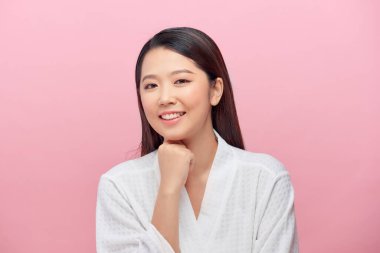 Temiz tenli, beyaz dişli, gülümseyen, elleri pembe arka planda, çenesinin altında tutan çekici bir kadın.