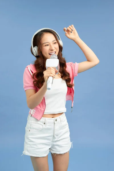 Beautiful Asian girl with microphone sings and headphone isolated over blue background.