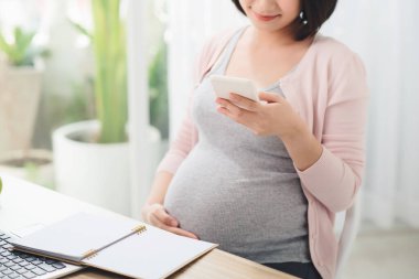Abdomen kızı üçüncü üç aylık dönemde ofiste akıllı telefonuyla çalışıyor. Çevrimiçi çalışıyor
