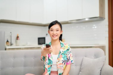 Kanepede uzanıp uzaktan kumandayla televizyon izleyen güzel bir kadın.