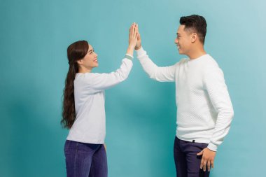 Dost canlısı genç kadın ve erkeğin görüntüsü. Basit giyinmiş, gülüyor ve mavi arka planda beşlik çakıyor.