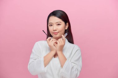 Pembe arka planda yalnız gülümseyen güzel bayan maskarayı elinde tut.