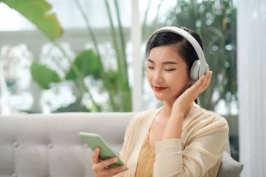 Evdeki kanepede dinlenirken müzik dinleyen genç bir kadın.