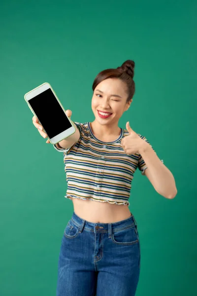年轻美丽的亚洲女人 穿着休闲装 站在绿色背景下 展示着空白屏幕手机 — 图库照片