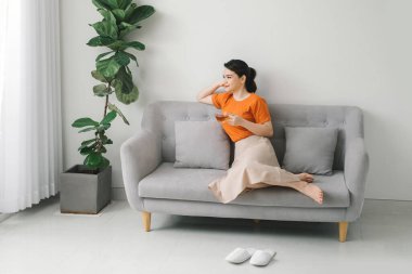 Çekici genç bir kadın evdeki kanepede dinlenirken bir fincan çay içiyor.