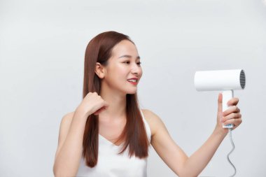 Güzel mutlu bir kadının portresi uzun saçlarını kurutma makinesiyle beyaz arka planda kurutuyor.