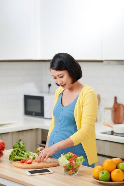 Hamile kadın mutfakta taze yeşil salata karıştırıyor..