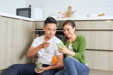 Yerde cep telefonuyla mutfakta oturan harika bir çiftin görüntüsü..