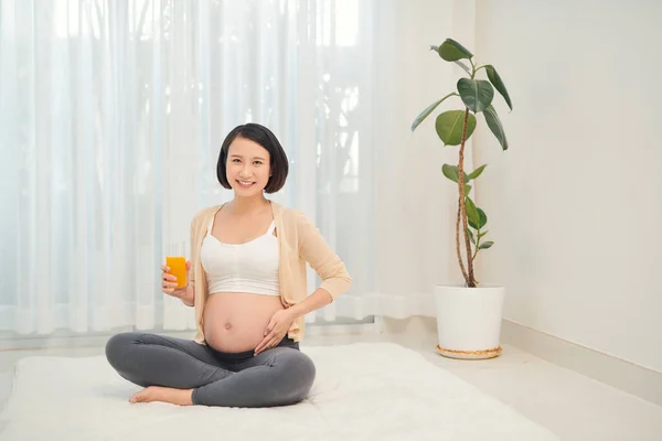 care about unborn child. pregnancy, healthy food and people concept, happy pregnant woman drink orange juice at home
