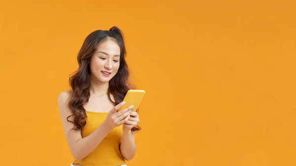 一个快乐的年轻女人站在黄色的背景下 用手机 — 图库照片