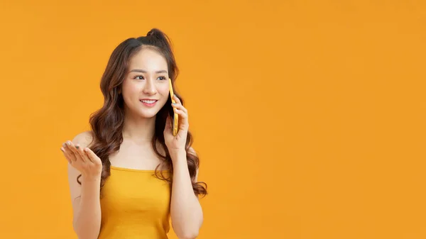 黄色の壁の背景の上に隔離されたポーズをとっている可愛いです笑顔アジアの女性のイメージ携帯電話によって話して — ストック写真