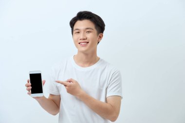 Gülümseyen Asyalı genç bir adamın portresi beyaz arka plandaki boş ekran cep telefonunu işaret ediyor.