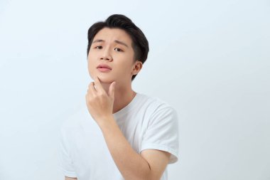 Beyaz arka planda genç yakışıklı bir adam kameraya kendinden emin bir şekilde bakıyor ve elleri çenesinde gülümsüyor. Olumlu düşünüyorum..