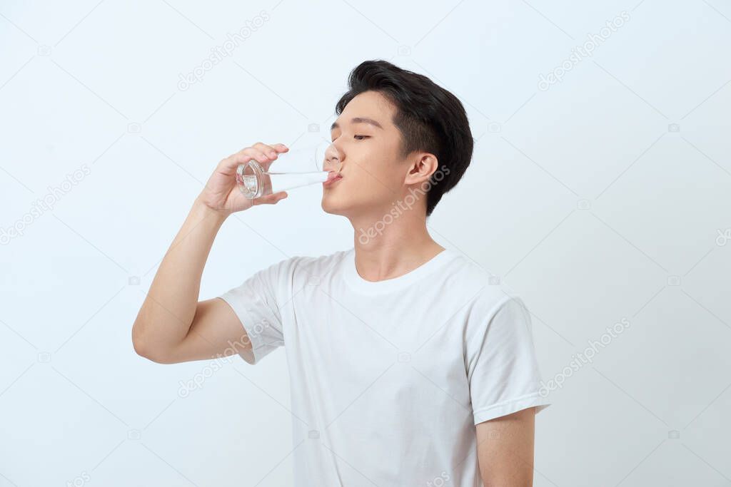 A man in a t-shirt and trousers on a white background drinking water from a glass