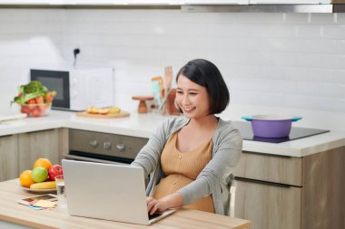 Mutfakta dizüstü bilgisayar kullanan güzel genç bir kadın.