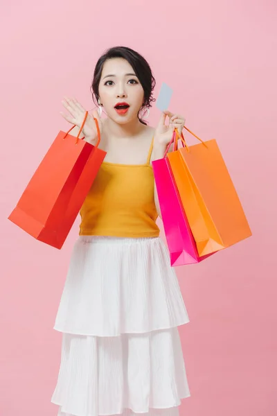 漂亮的年轻姑娘穿着休闲装 孤零零地站在粉红的背景下 提着购物袋 拿着信用卡 — 图库照片