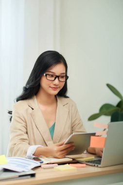 Günlük kıyafetli neşeli bir gazetecinin portresi. Masada oturmuş, elinde aletle interneti kullanıyor.