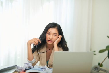 Dizüstü bilgisayarla çalışan genç Asyalı kadın. Bir kadın evde çalışırken bir fikir üretir ve stres hisseder.