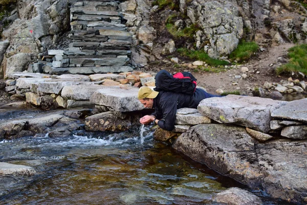 Tourist drinks clean, meltwater from a stream flowing near a path to Kjeragbolten. Norway is one of few countries in world where there is a sufficient amount of pure drinking fresh water in nature.