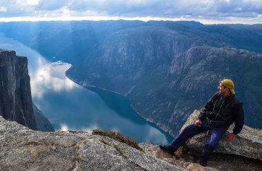 Lysefjorden 'ın yukarısındaki adamımız. Kjeragbolten 'in yakınlarda bulunduğu mavi sulara yansıyan bulutlarla muhteşem dağ manzarası. Norveç, Kjerag platosundan görüntü.