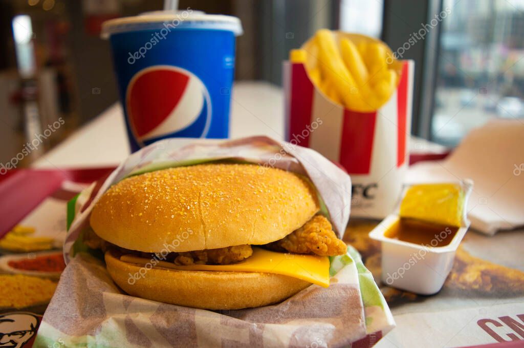 Kiev, Ukraine - March 8, 2020: Food and drink in a popular fast food restaurant KFC. Is popular fast food chain known as Kentucky Fried Chicken. Potato fries, Pepsi and burger with curry sauce.