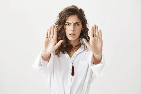 Worried and confident caucasian woman showing stop or do not come closer gesture with hands, frowning and expressing dislike, standing against gray background. Girl says ex stay far from her