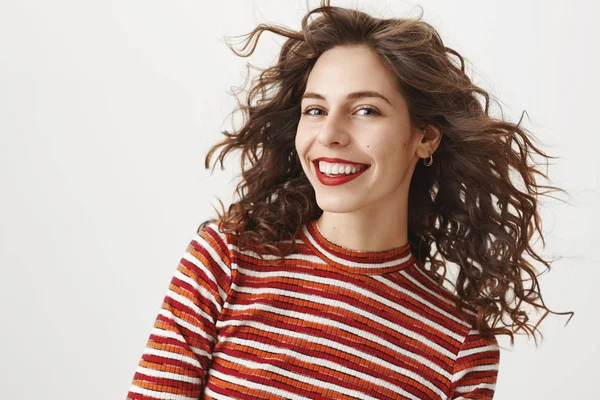 Waist-up shot of carefree fashionable woman with curly hair and red lipstick, smiling broadly, gazing happily at camera. Girlfriend dressed in stylish outfit, walking to party, ready impress everyone