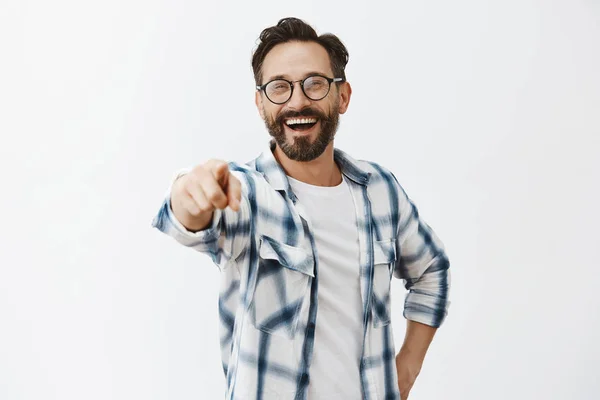 Haha got you. Portrait of carefree funny and emotive handsome mature coworker with beard in checked shirt and glasses, pointing at camera with index finger and laughing over out loud, being rude