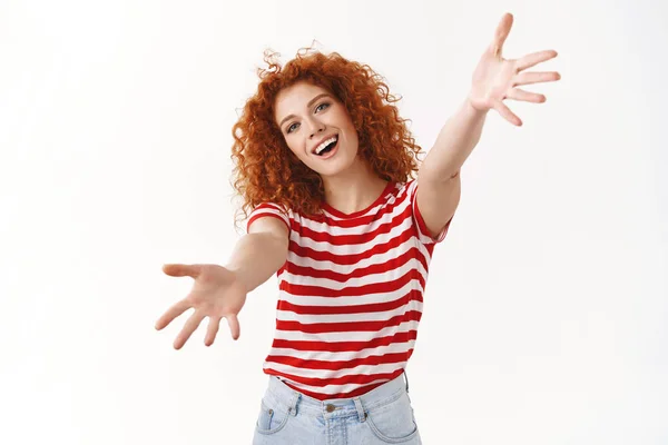 Come on free hugs. Charming friendly attractive curly redhead girl inviting cuddle stretch hands forward camera wanna hold you take product tilting head smiling broadly feel excited, white background