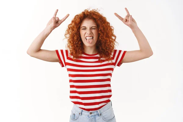 Heavy metal rock party. Playful carefree happy redhead curly-haired young outgoing woman close eyes show tongue thrilled raise hands rock-n-roll gesture having fun awesome music concert