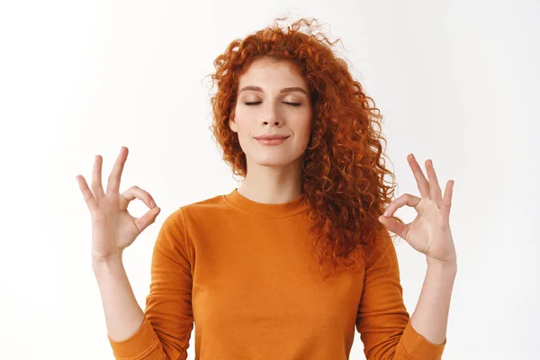 Redhead girl calm down, soothing stress with yoga. Relieved happy ginger woman peacefully meditating, making zen mudra sign, breathing patient, smiling tenderly, inhale positive vibes