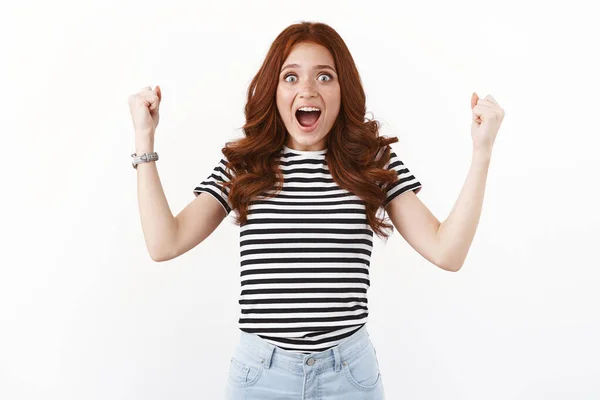 Surprised excited and happy young redhead woman found out she won lottery, pump fists up air, stare camera gasping at unbelievable awesome news, triumphing, celebrating victory, white background