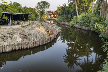 Küçük kanal ve patikalardan oluşan karmaşık bir ağın parçası olan dolambaçlı bir su yolu, yemyeşil bitki örtüsü, biyolojik çeşitlilikteki doğal yaşam alanları ve tarım arazileri aracılığıyla sakinlerin küçük ahşap evlerinin önünden geçiyor..