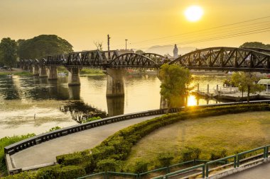 The setting sun pours warm golden light across the famous landmark,part of the infamous Thai-Burma Death Railway route,visited by many tourists every day.
