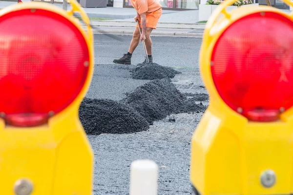 Road workers distribute the hot asphalt with shovels on the road, Germany