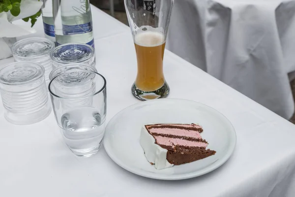 A piece of wedding cake on a plate with a glass of water and a wheat beer