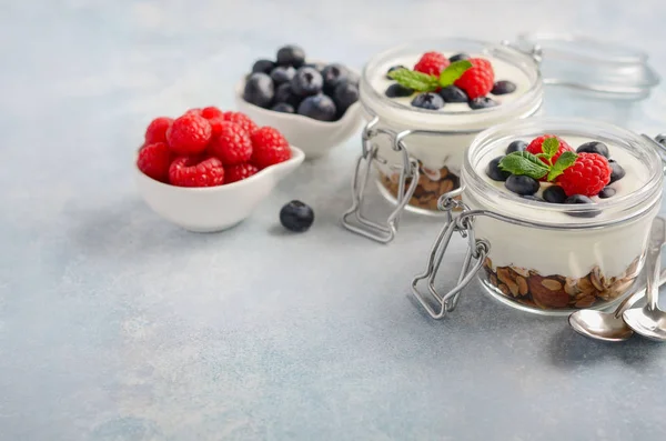 青いコンクリート背景 健康的な朝食の概念 セレクティブ フォーカス コピー領域に Jar の自家製グラノーラとガラスの新鮮な果実とヨーグルトのパフェ — ストック写真