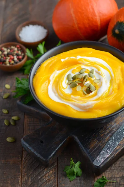 Pumpkin cream soup with cream and pumpkin seeds on rustic wooden table.