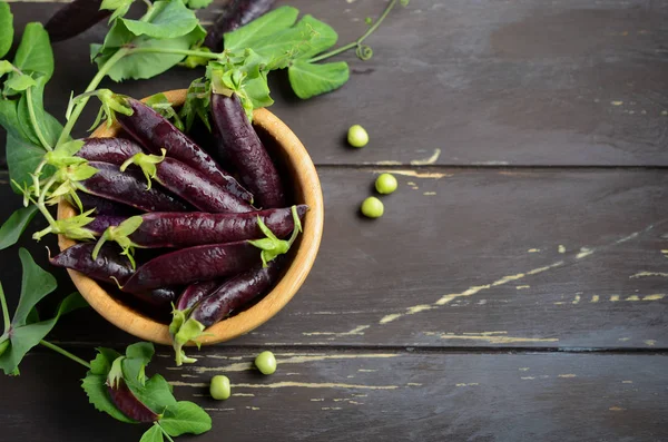 Taze organik mor yeşil bezelye rustik ahşap masa üzerinde bir ahşap kase.