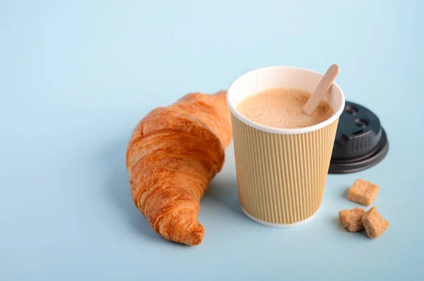 Take away coffee cup and croissant on blue background.