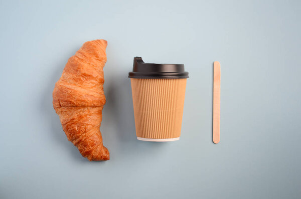 Take away coffee cup and croissant on blue background, top view, flat lay, copy space.