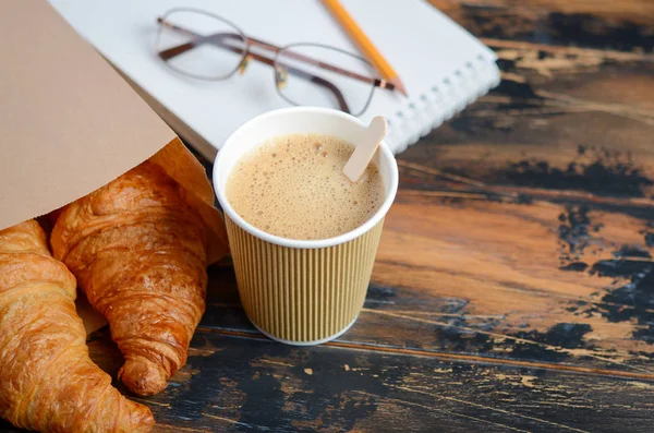 Take away coffee cup with croissant on wooden table.