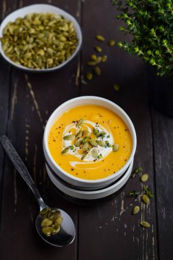 Karanlık rustik ahşap masa üzerinde krem ve kabak çekirdeği ile kabak kremalı çorba.