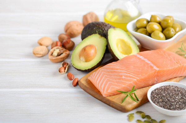 Selection of healthy unsaturated fats, omega 3 - fish, avocado, olives, nuts and seeds, selective focus.