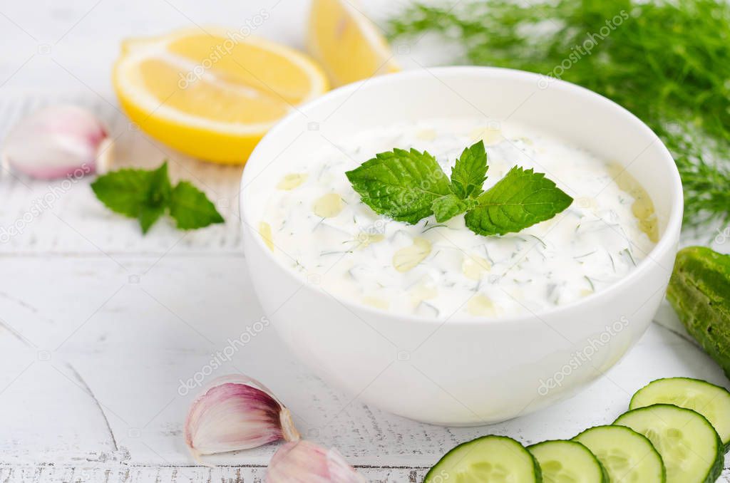 Greek dip sauce or dressing tzatziki decorated with olive oil and mint on white wooden table 