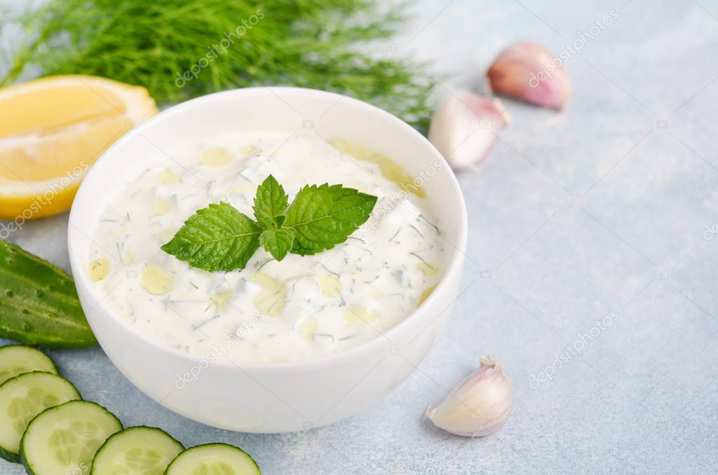 Greek dip sauce or dressing tzatziki decorated with olive oil and mint on blue background.